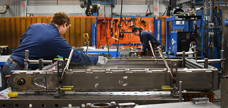 Manufacturing workers preparing steel pieces for welding.